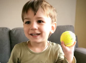 A young boy holds a tennis ball in his left hand, in a story about left-handedness revealing family history.